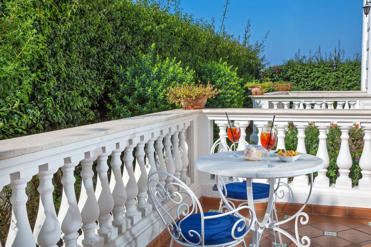 A balcony with white balustrades, a round table with two chairs, and potted plants.