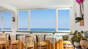 Un comedor con dos mesas, sillas amarillas y vistas al mar a través de amplios ventanales.