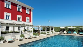 Una piscina al aire libre, sombrillas, sillones reclinables de piscina