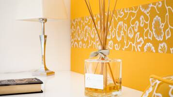 A clear glass bottle of perfume with a label, a book, and a lamp on a white surface.