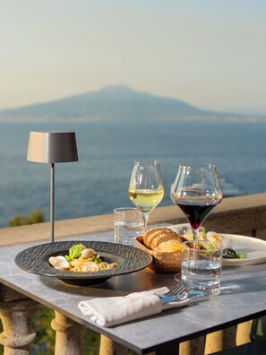 A table with a plate of food, two glasses of wine, and a lamp, set against a scenic mountain backdrop. - Hotel Villa Garden (Sant'Agnello)