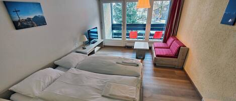 Habitación de hotel con dos camas, televisión, una mesita y un sofá.