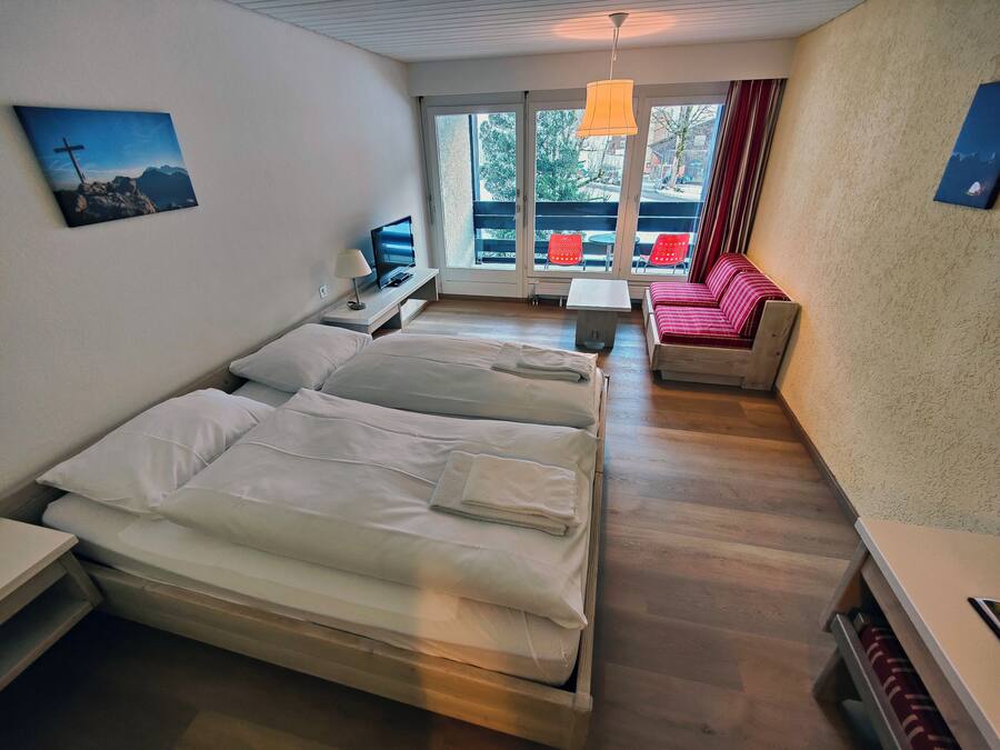 Habitación de hotel con dos camas, televisión, una mesita y un sofá.