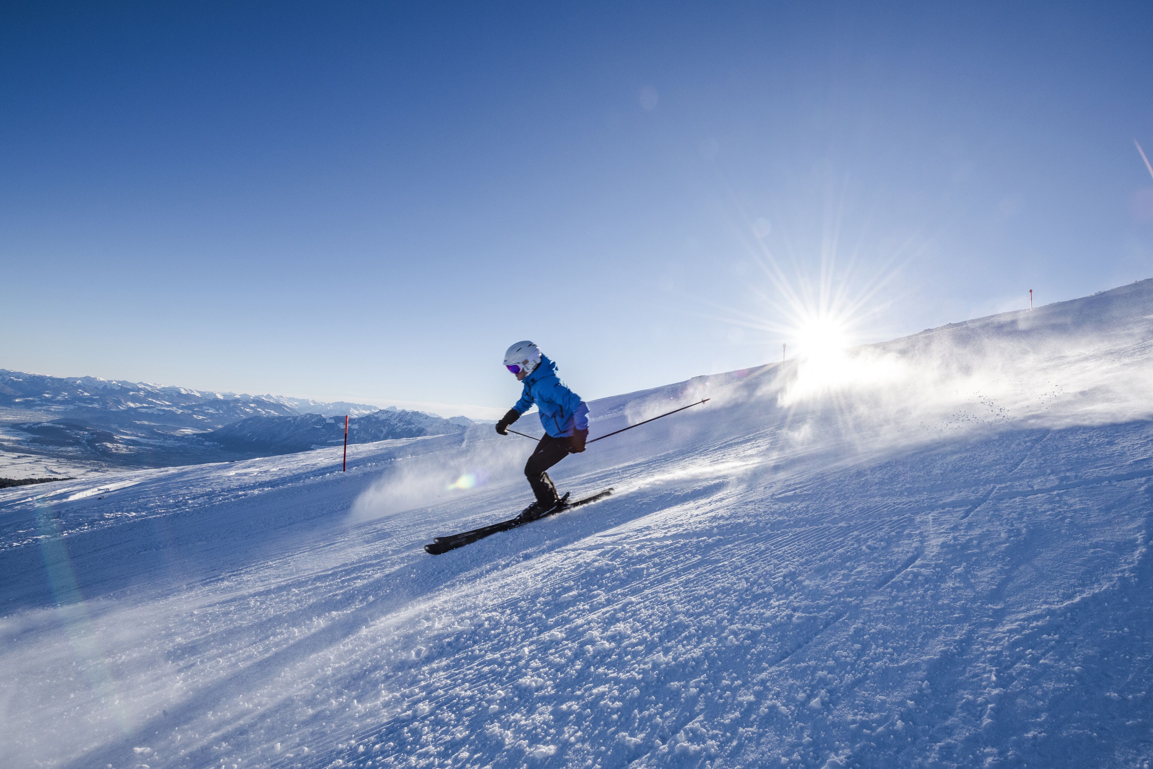 A skier on a snowy slope with a clear sky and distant mountains.
