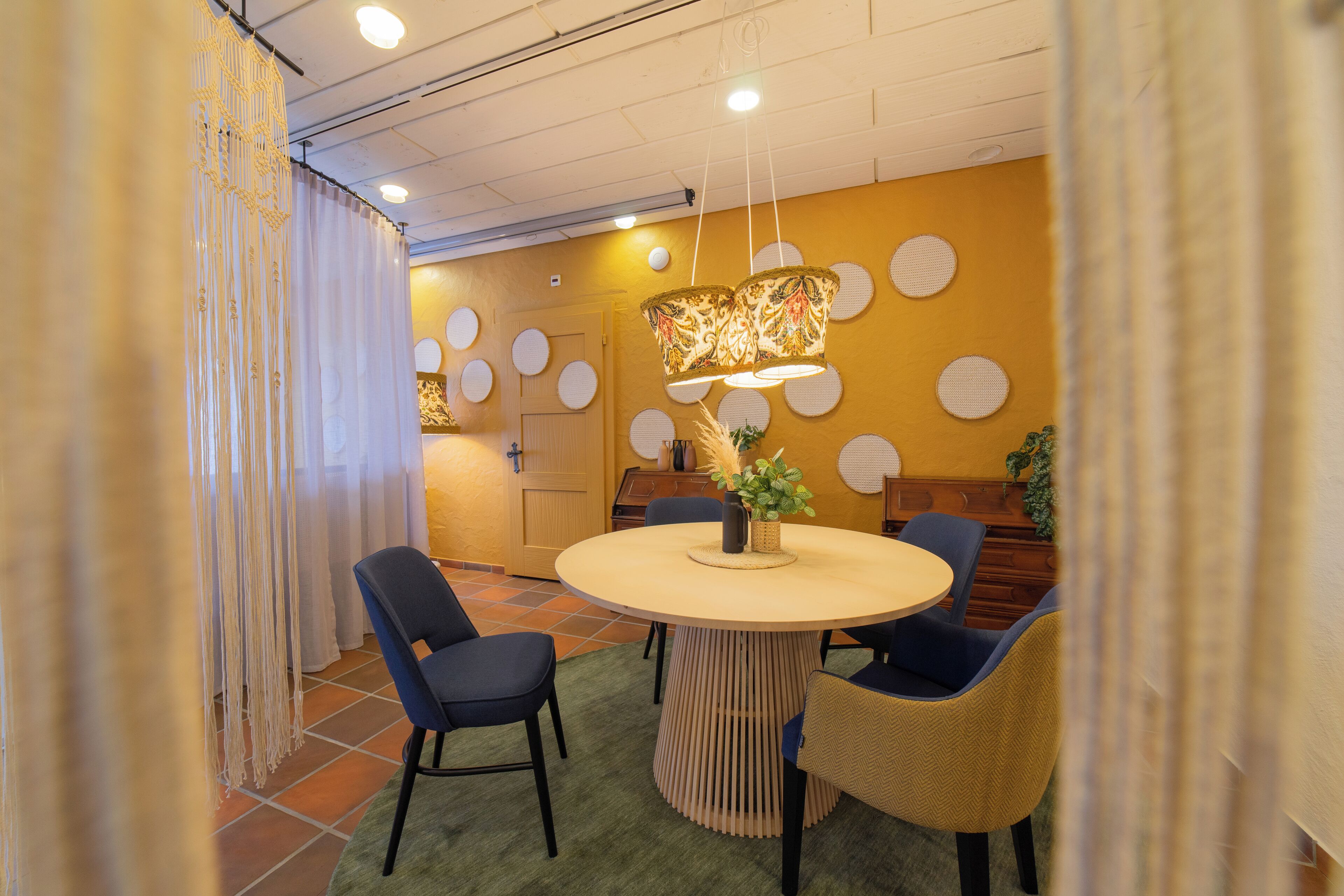 A dining area with a round table, blue chairs, and a decorative hanging light fixture.