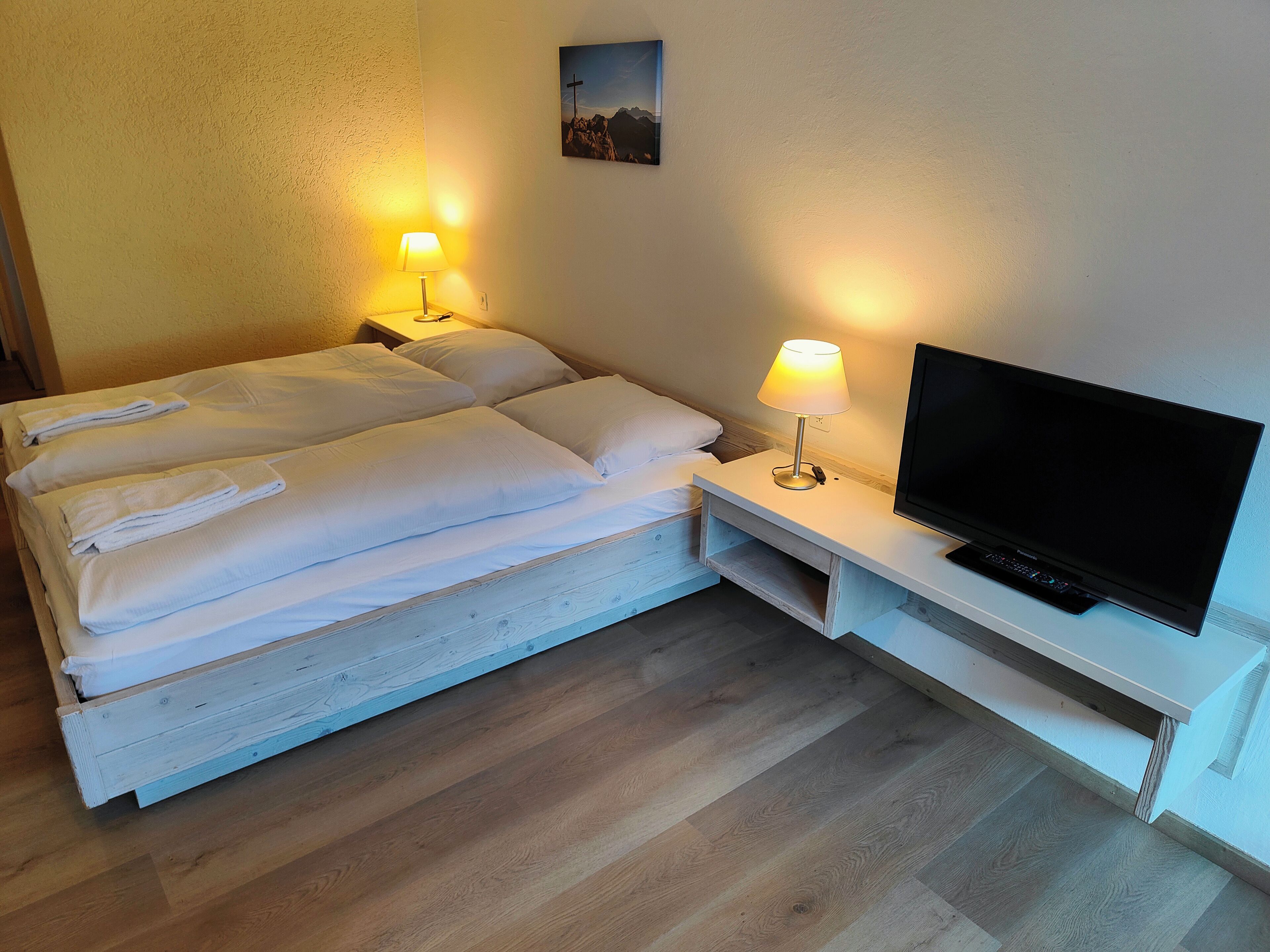 Una habitación de hotel con una cama, dos lámparas de noche, un televisor y un cuadro en la pared.