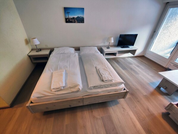 A double bed with white linens, a TV on a stand, a lamp, and a painting on the wall.