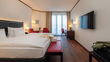 A hotel room with a bed, a desk, a chair, a TV, and a window with curtains.