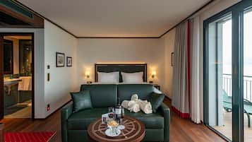 A modern hotel room with a large bed, a green sofa, a round coffee table, and a view through a large window.