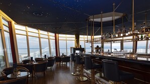 Un bar con vistas al mar, con suelo de madera y taburetes de bar modernos.