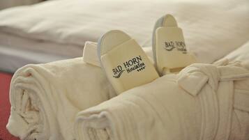 Ein ordentlich gefaltetes weißes Handtuch mit dem Logo des Bad Horn Hotel & Spa, platziert auf einem Bett mit rotem Kopfteil.