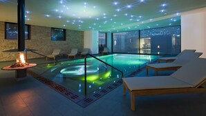 Un área de piscina interior moderna con un elemento decorativo de fuego, sillones de descanso y vistas a la ciudad.