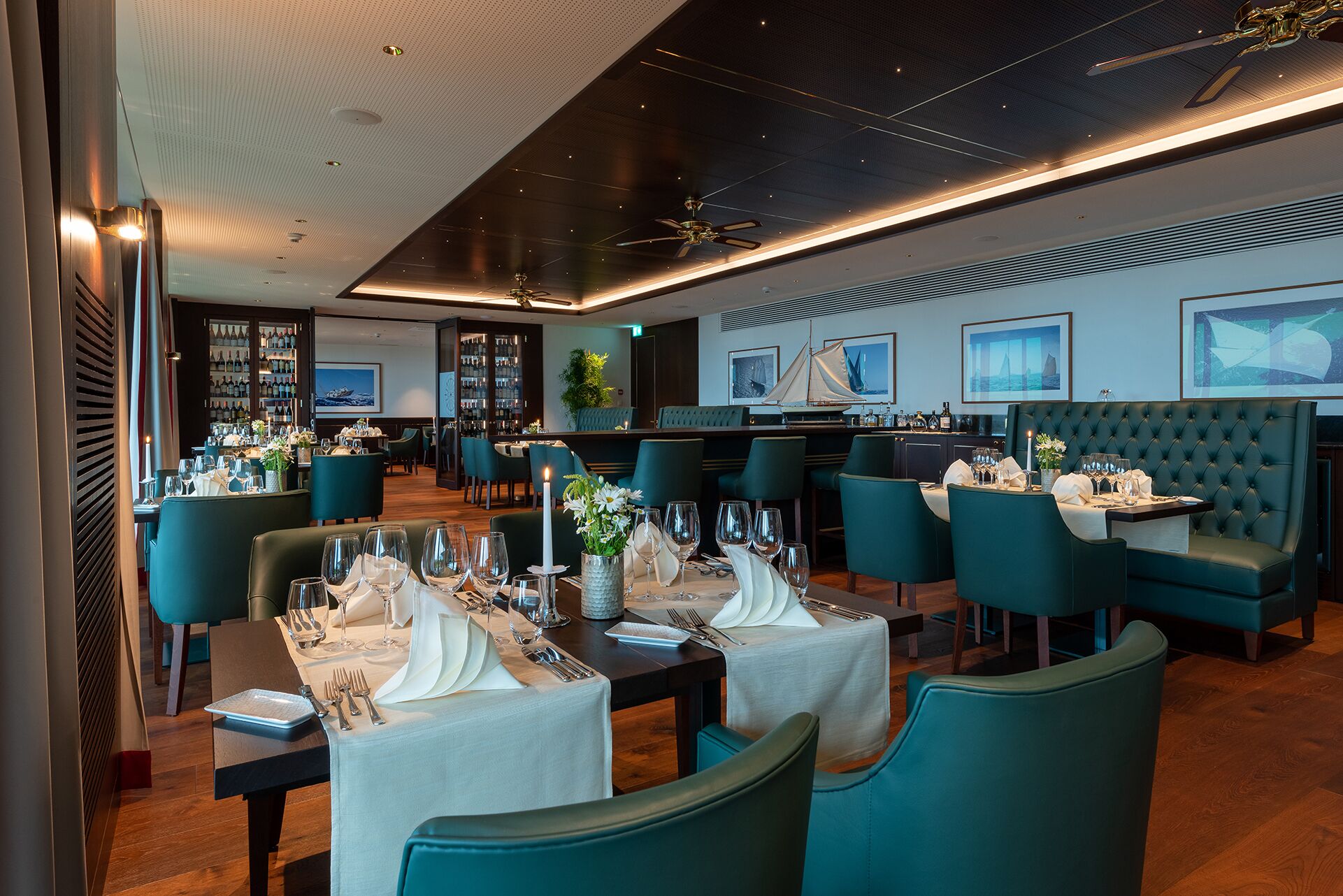 A restaurant with teal chairs, white tablecloths, and a bar area.