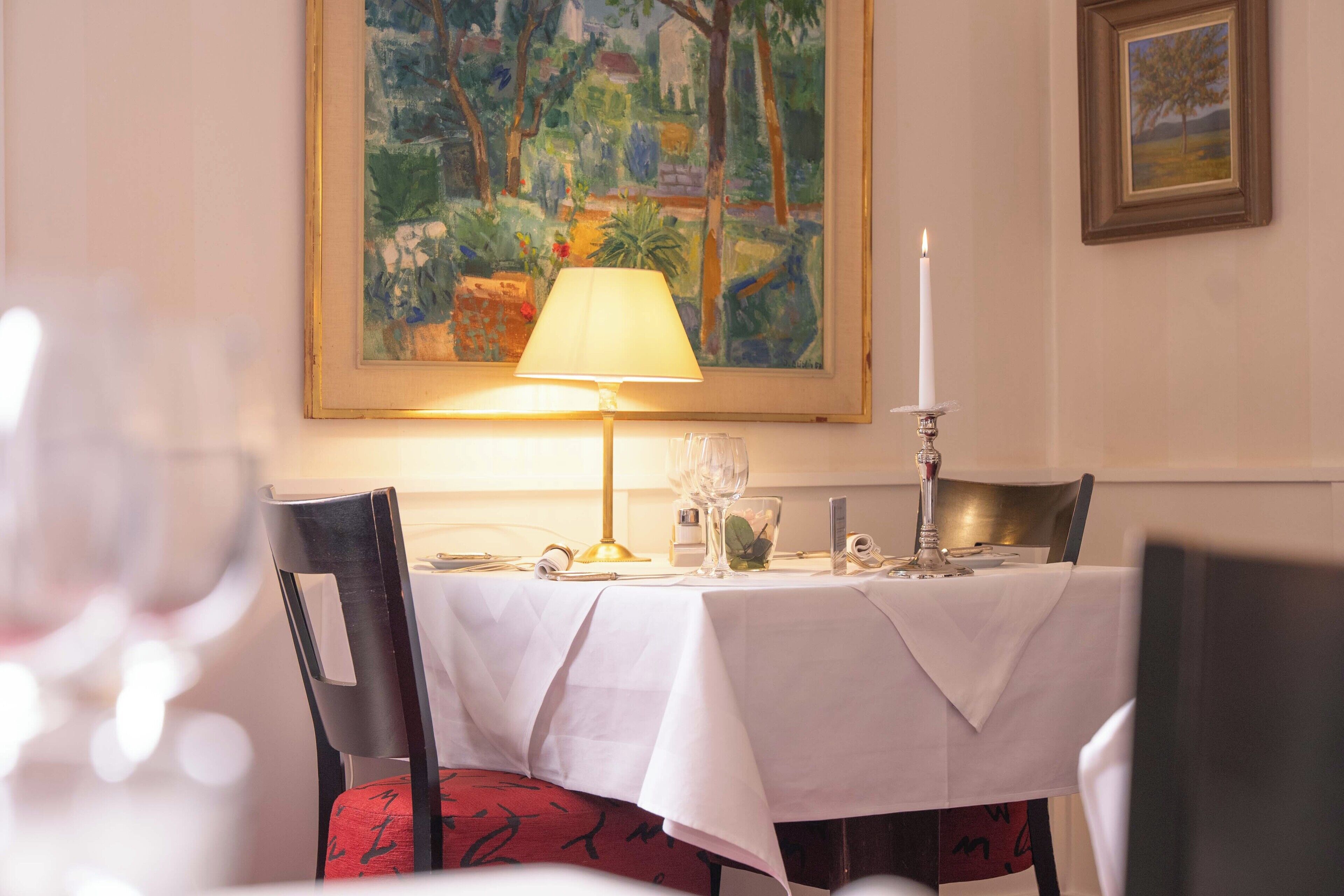 A dining table set with a white tablecloth, a candle, and a painting above.