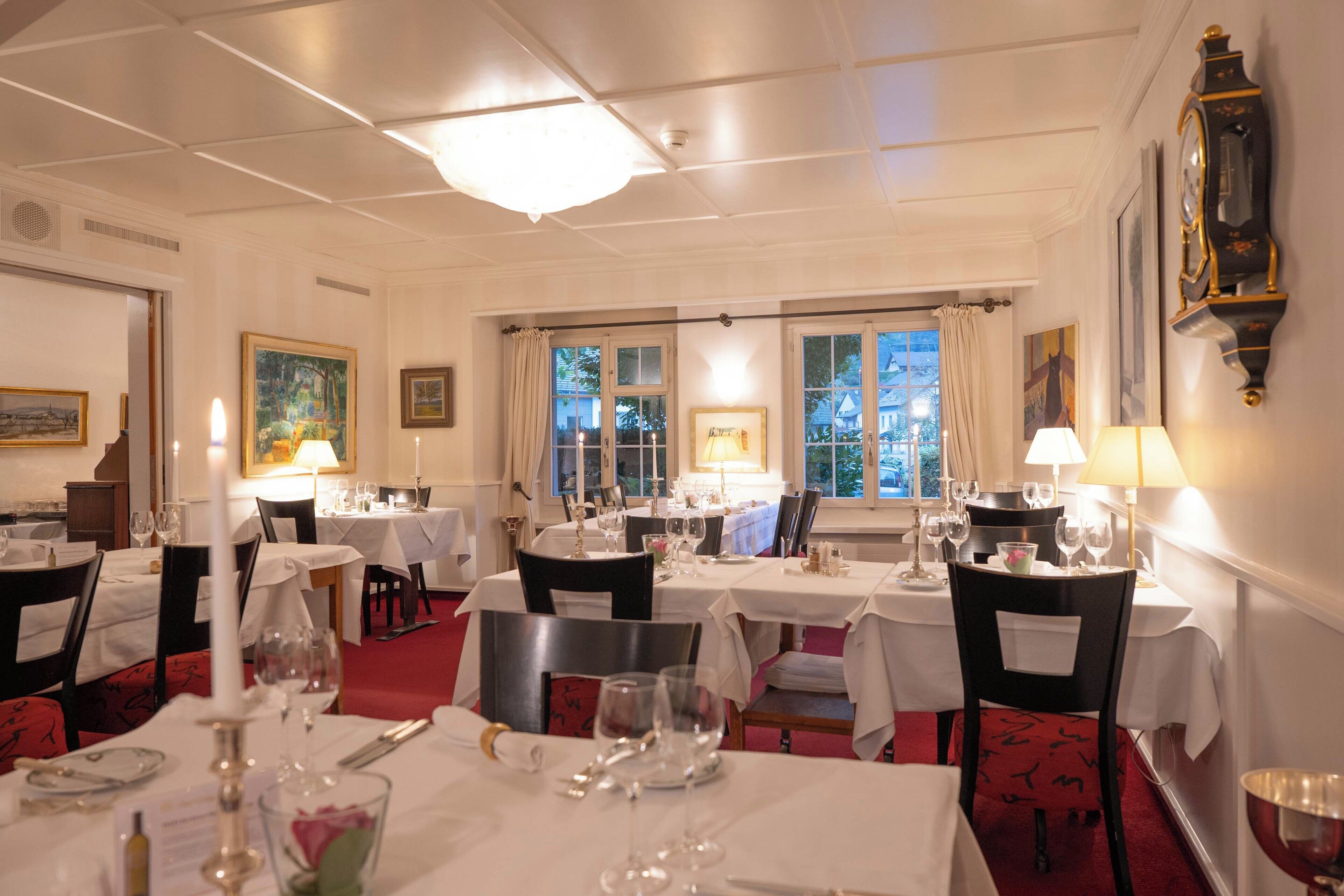 A dining area with multiple tables set for service, each with a white tablecloth and candle centerpiece.