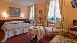 A hotel room with a large bed, a small table with a bottle and glasses, a chair, and a television. - Bad Eptingen (Eptingen)