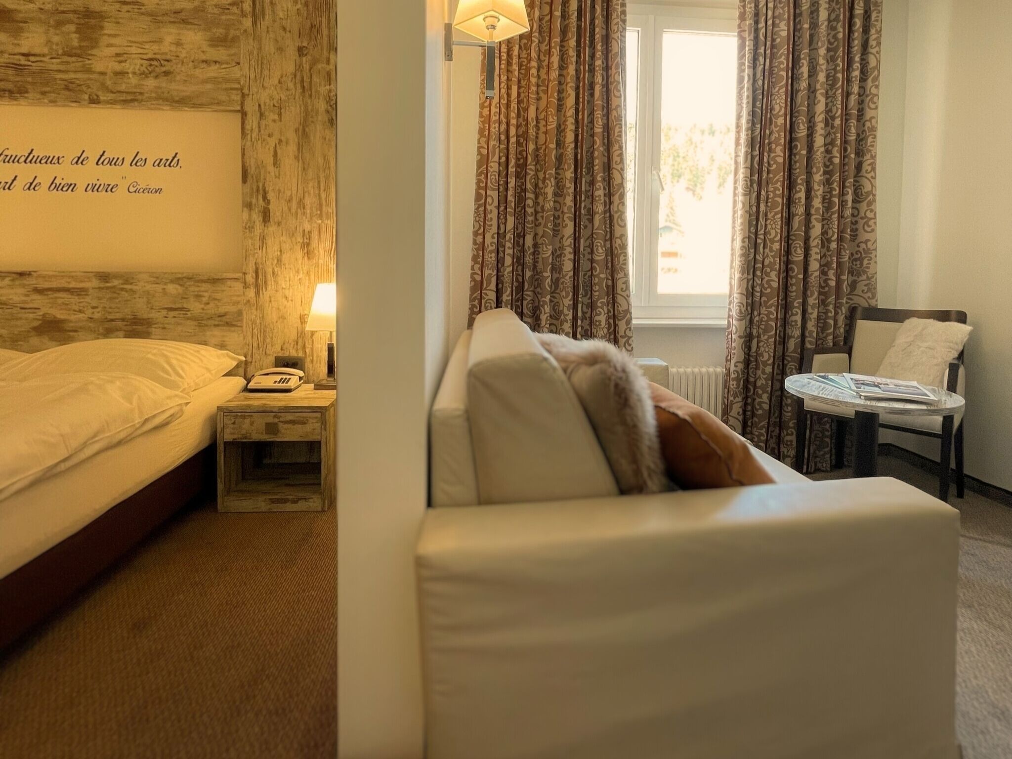 A hotel room with a bed, a nightstand, a lamp, a chair, and a window with curtains.