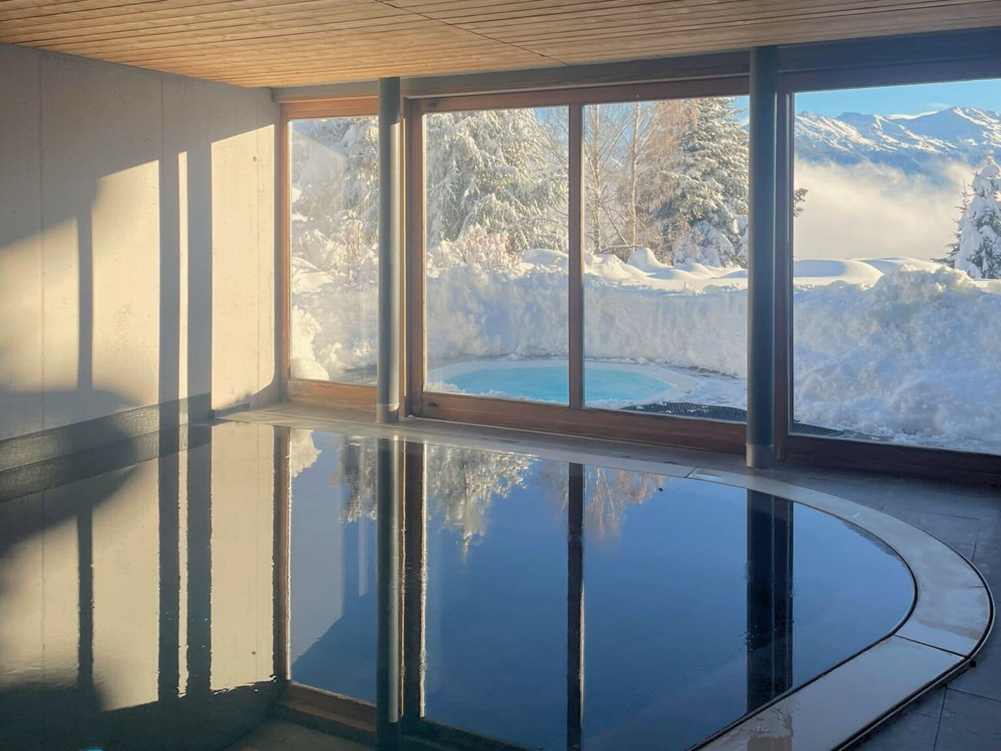 Une pièce dotée d’une grande fenêtre donnant sur un paysage enneigé et une piscine.