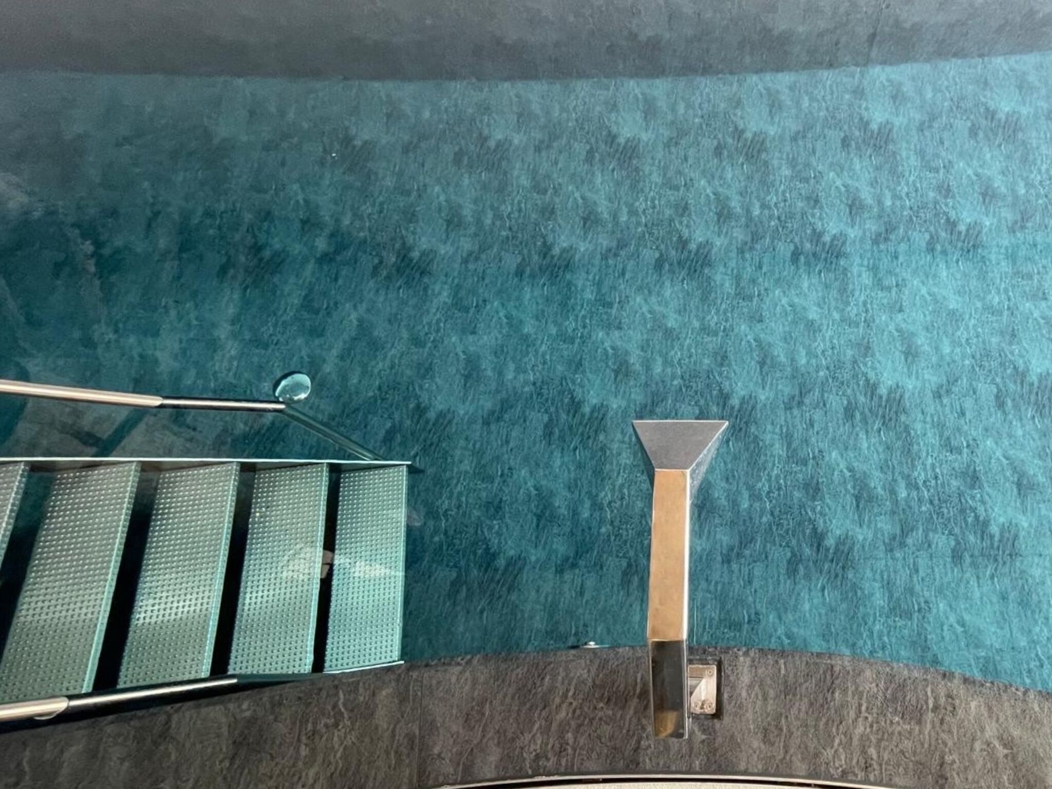 A staircase with a metal handrail and a glass balustrade against a textured teal wall.