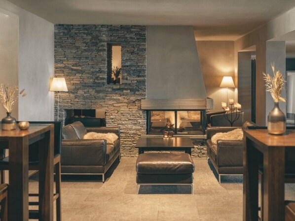 Una sala de estar moderna con pared de piedra, sofás de cuero, chimenea y un espejo grande.