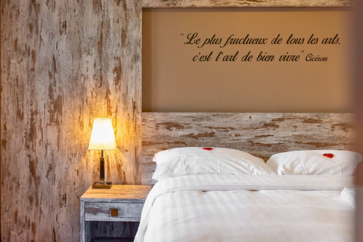 Une chambre à coucher avec une tête de lit en bois rustique, une lampe de chevet et une citation écrite sur le mur en français.