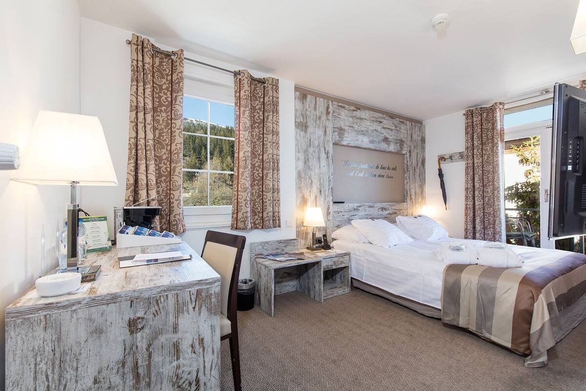 Une chambre d’hôtel comprenant un lit, des tables de chevet, un bureau avec une lampe, une chaise et une vue sur l’extérieur.