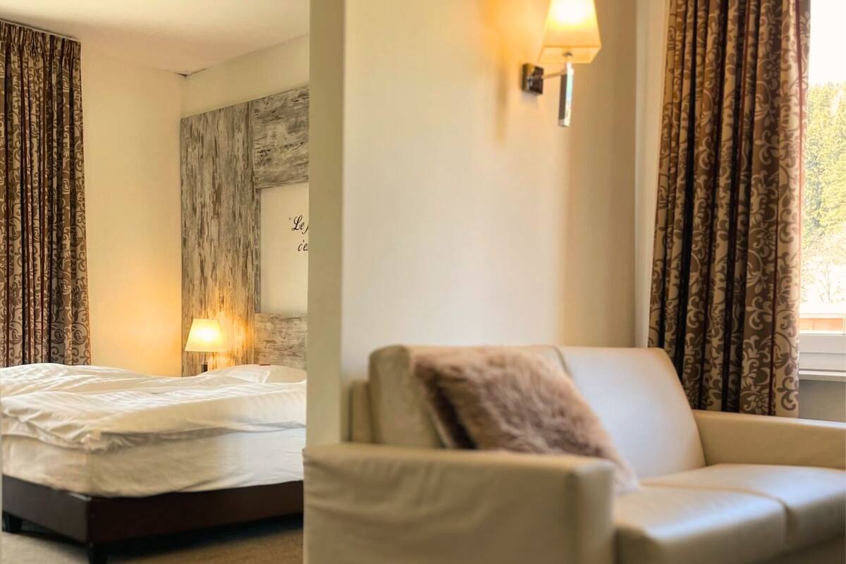 Une chambre d’hôtel avec un lit, un canapé, une lampe fixée au mur et des rideaux.