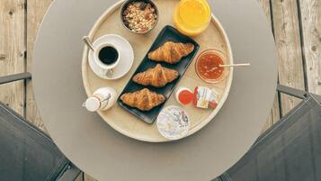 Ein runder Tisch mit einer Tablett, auf dem Croissants, eine Tasse Kaffee, ein Glas Orangensaft und Beilagen stehen.