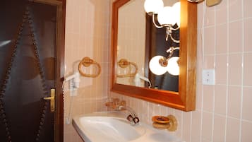Un baño con lavamanos blanco, puerta de madera y espejo con iluminación.