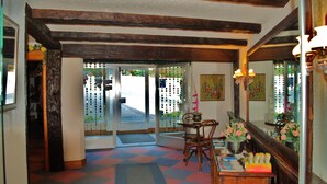 A hotel lobby with a checkered floor, wooden beams, a reception desk, and a door leading outside. - Astoria (Leukerbad)