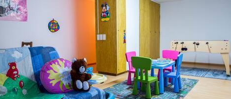 Un cuarto de juegos infantil con una cama, sillas de colores, una mesita pequeña y un juego de futbolín de juguete.