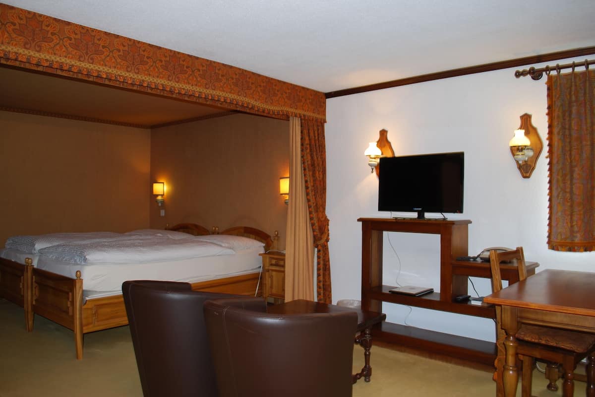 Habitación de hotel con una cama grande, un escritorio, una silla, un televisor y dos lámparas fijadas a la pared.