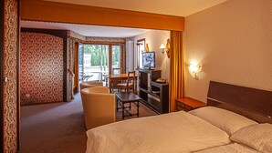 A hotel room with a bed, a desk with a television, a chair, and a small table. - Astoria (Leukerbad)