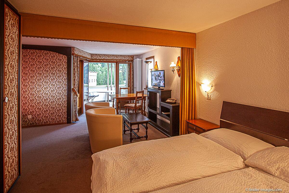 Una habitación de hotel con una cama, un escritorio con televisor, una silla y una mesita.
