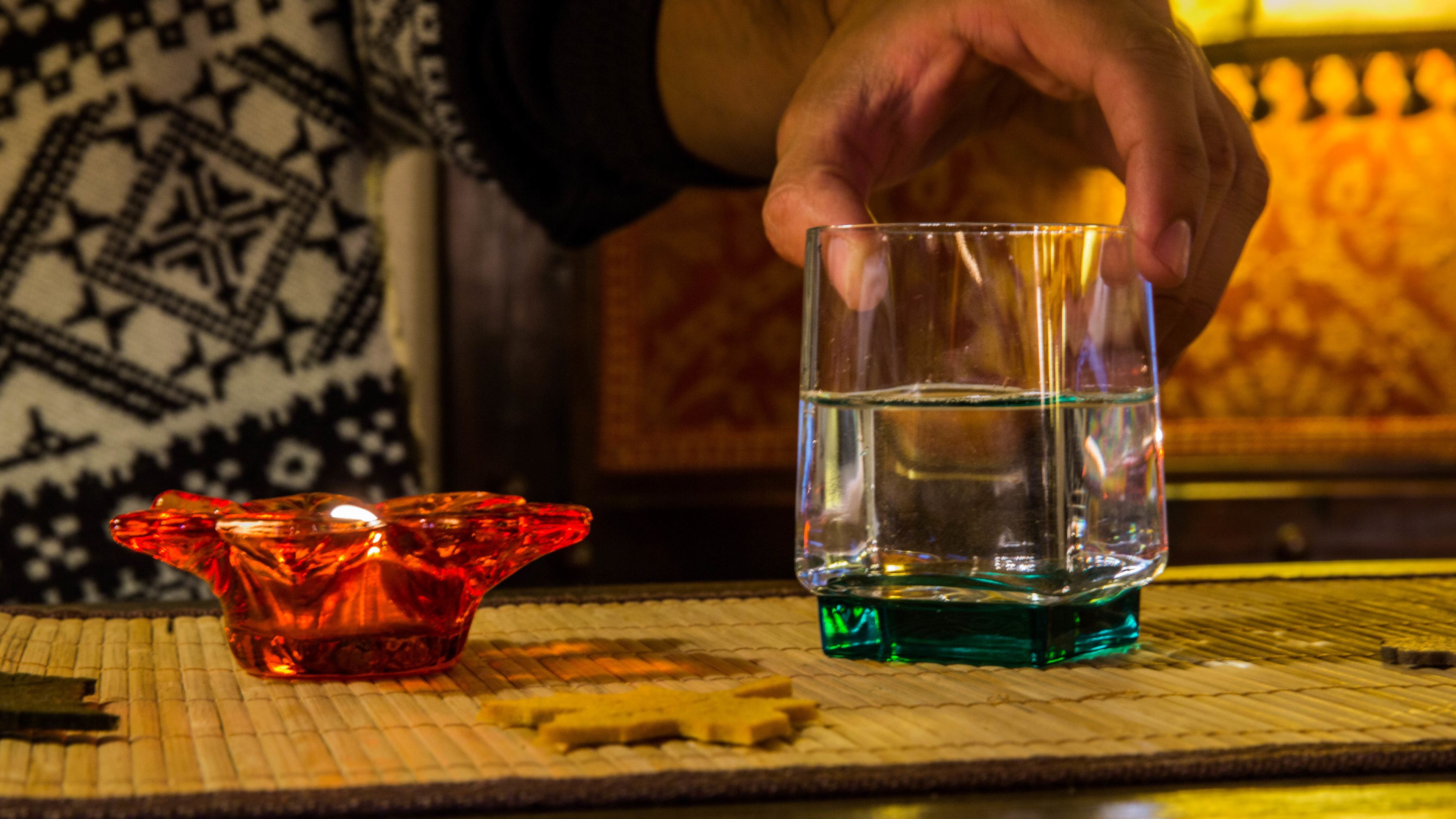 A hand holding a glass of water over a candle holder.