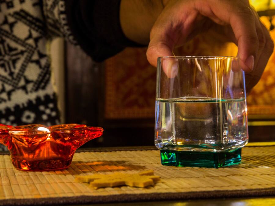 A hand holding a glass of water over a candle holder.