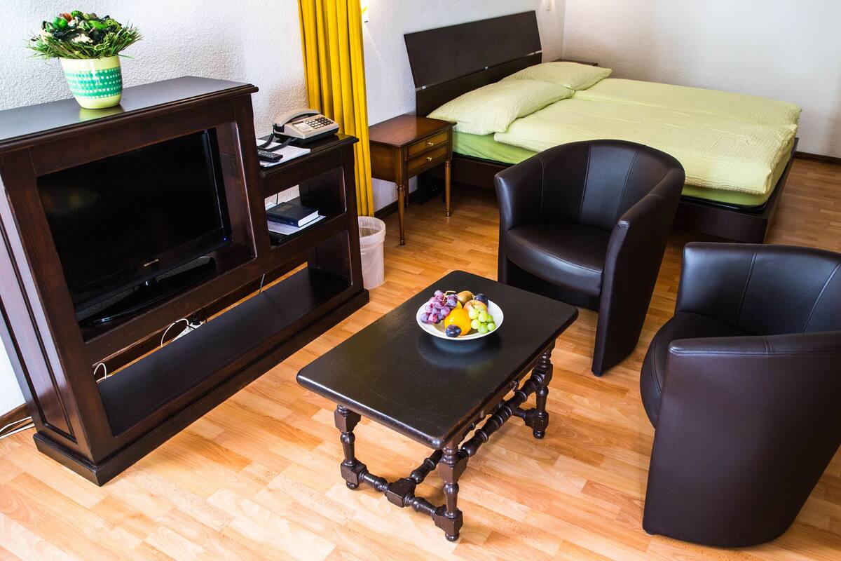 Una habitación de hotel compacta con una cama, un televisor, una pequeña mesa con fruta y dos sillas.