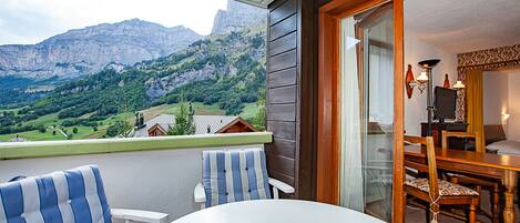 A balcony with a view of mountains, a dining area with a table and chairs, and a window with curtains.