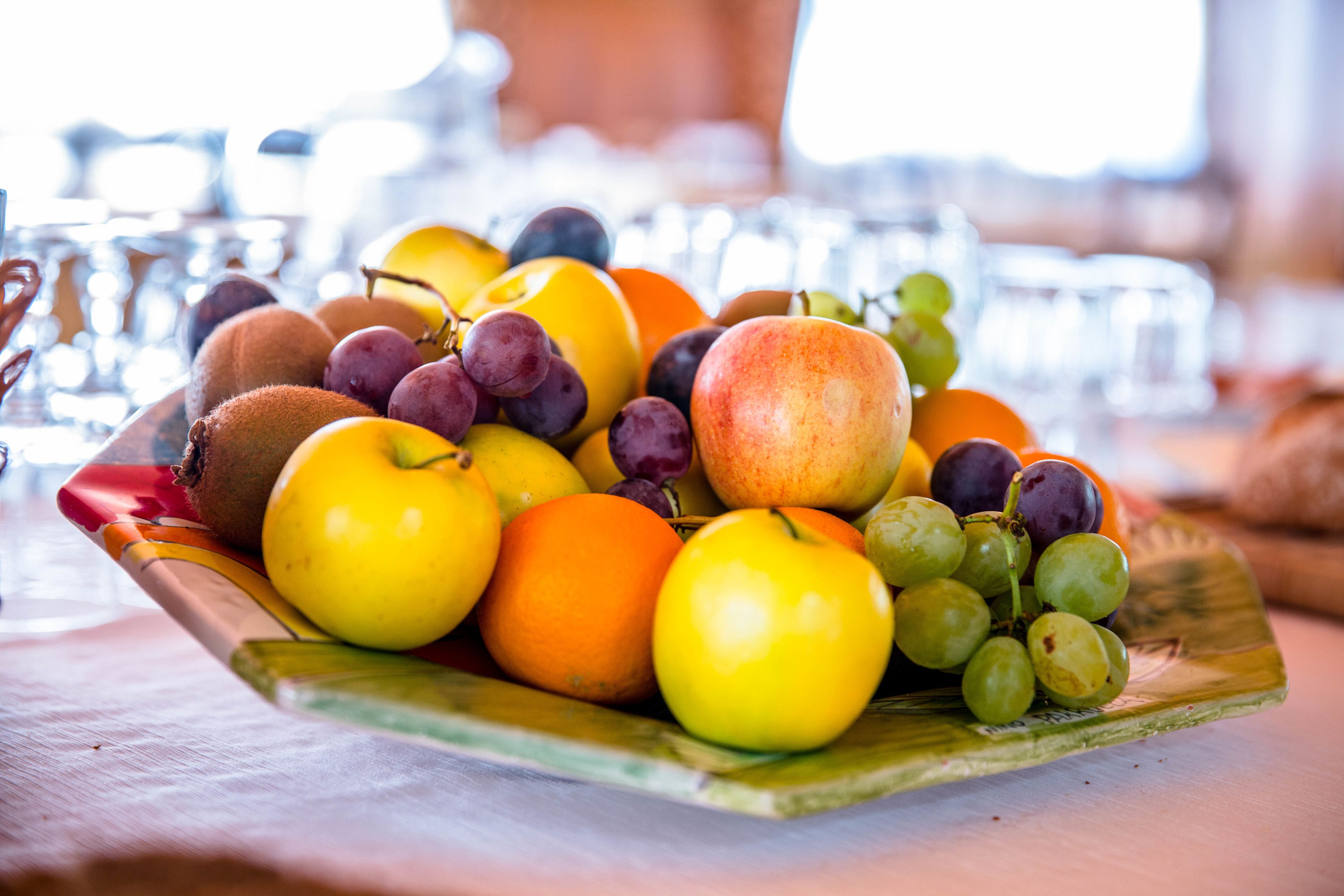 Eine Obstschale auf einem Tisch mit verschiedenen Früchten, darunter Äpfel, Orangen und Trauben.