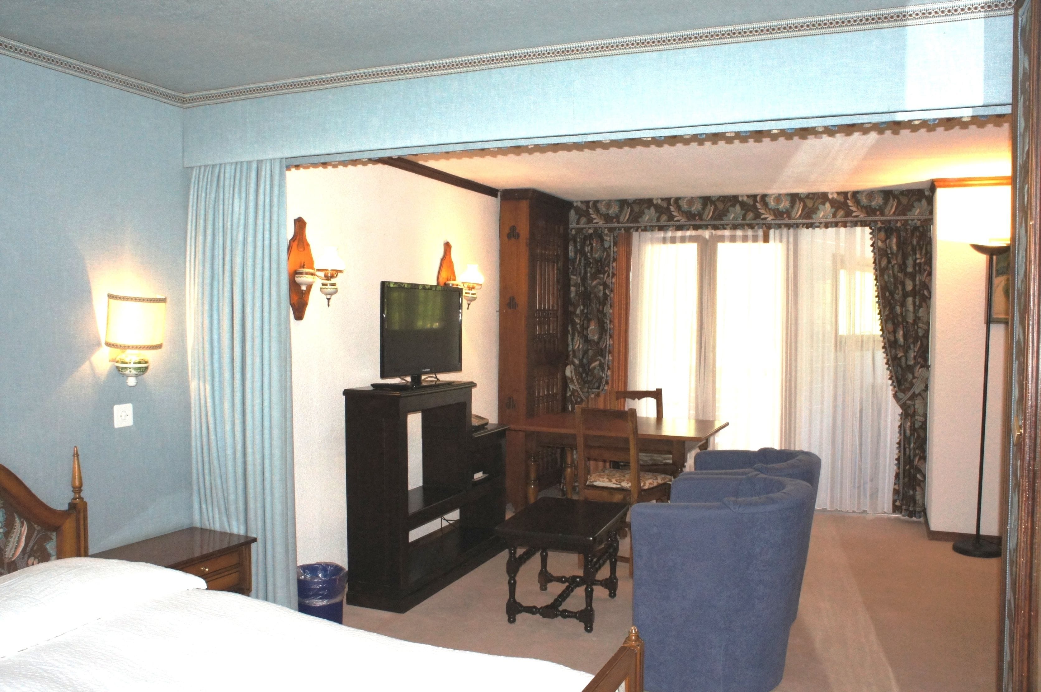 A hotel room with a bed, a desk, a television, a chair, and a window with curtains.