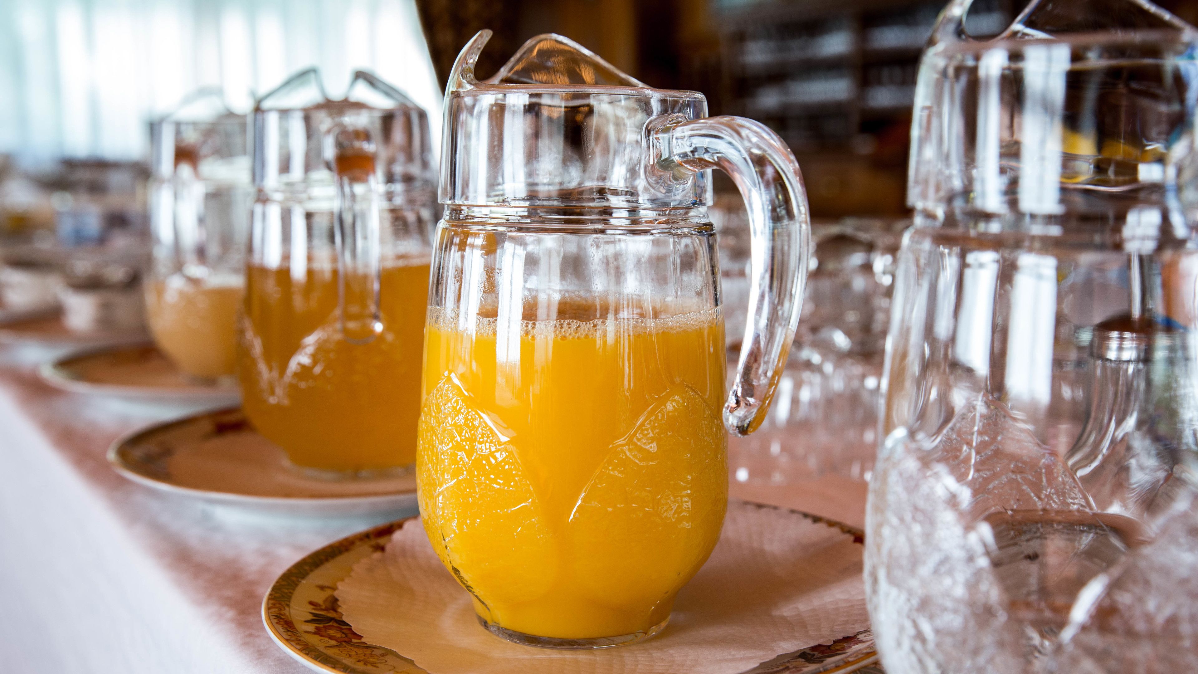 Diverses carafes de vidre transparent amb mànecs, plenes d'un líquid groc-taronja, probablement suc, damunt plats.