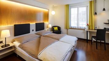Habitación de hotel moderna con una cama grande, mesitas de noche con lámparas, un escritorio con silla y una ventana con cortinas.