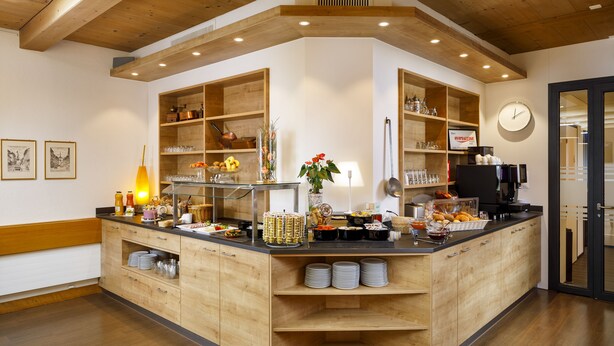 A modern kitchen with wooden cabinets, a central island, and various kitchen appliances. - Hotel Jardin (Bern)