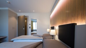 A hotel room with two beds, a wooden accent wall, and a nightstand with lamps. - Hotel Jardin (Bern)