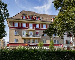 A multi-story hotel with red shutters, balconies, and a garden sign.