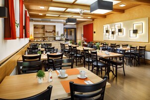 A spacious restaurant with multiple tables and chairs, wooden flooring, and a modern ceiling design.