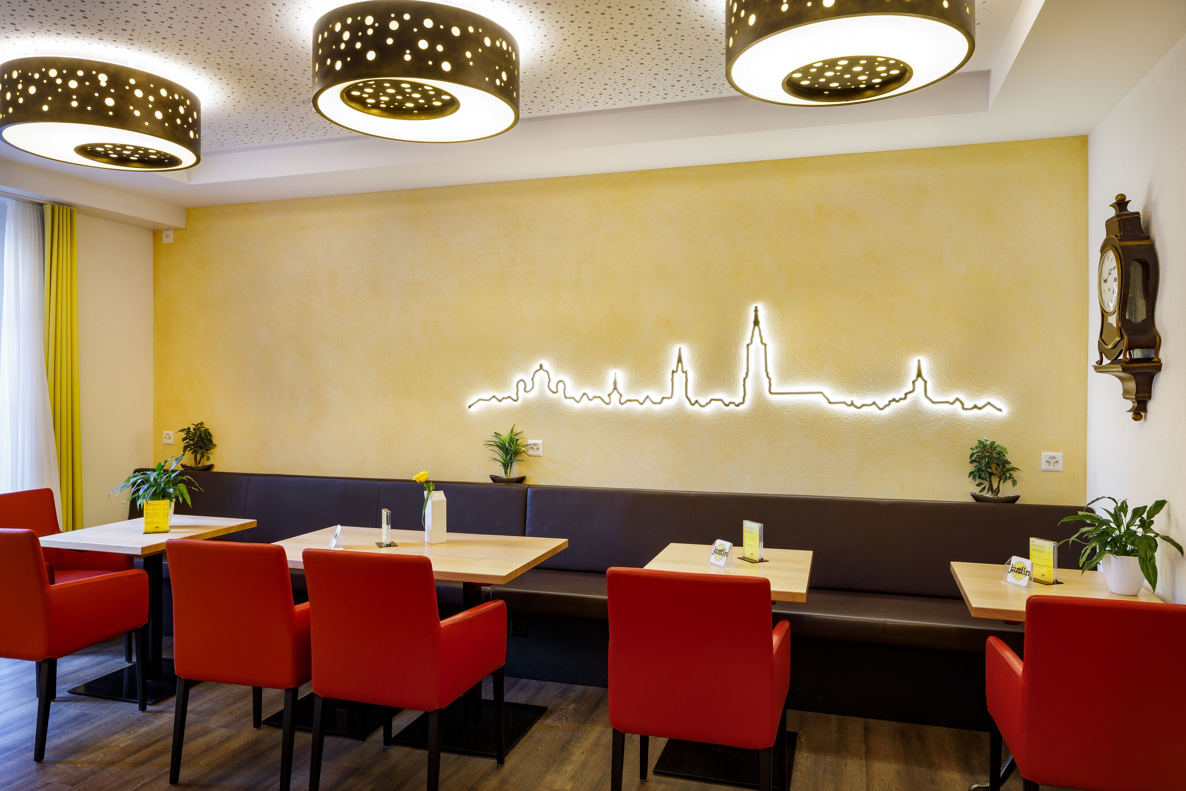 A restaurant with red chairs, wooden tables, and a neon city skyline on the wall.