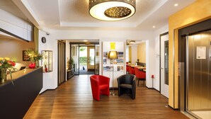A hotel lobby with a wooden floor, red and black chairs, a reception desk with a vase of flowers, and an elevator. - Hotel Jardin (Bern)