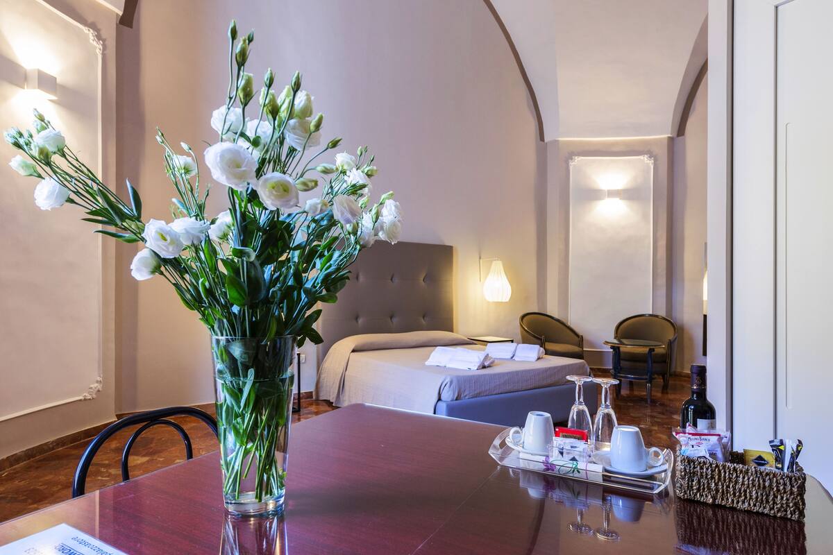 A hotel room with a bed, bedside table, and a dining area with a table set for two.