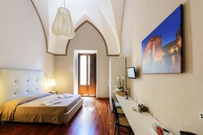 A hotel room with a large bed, a desk with a computer, a TV, and a painting of a bridge.